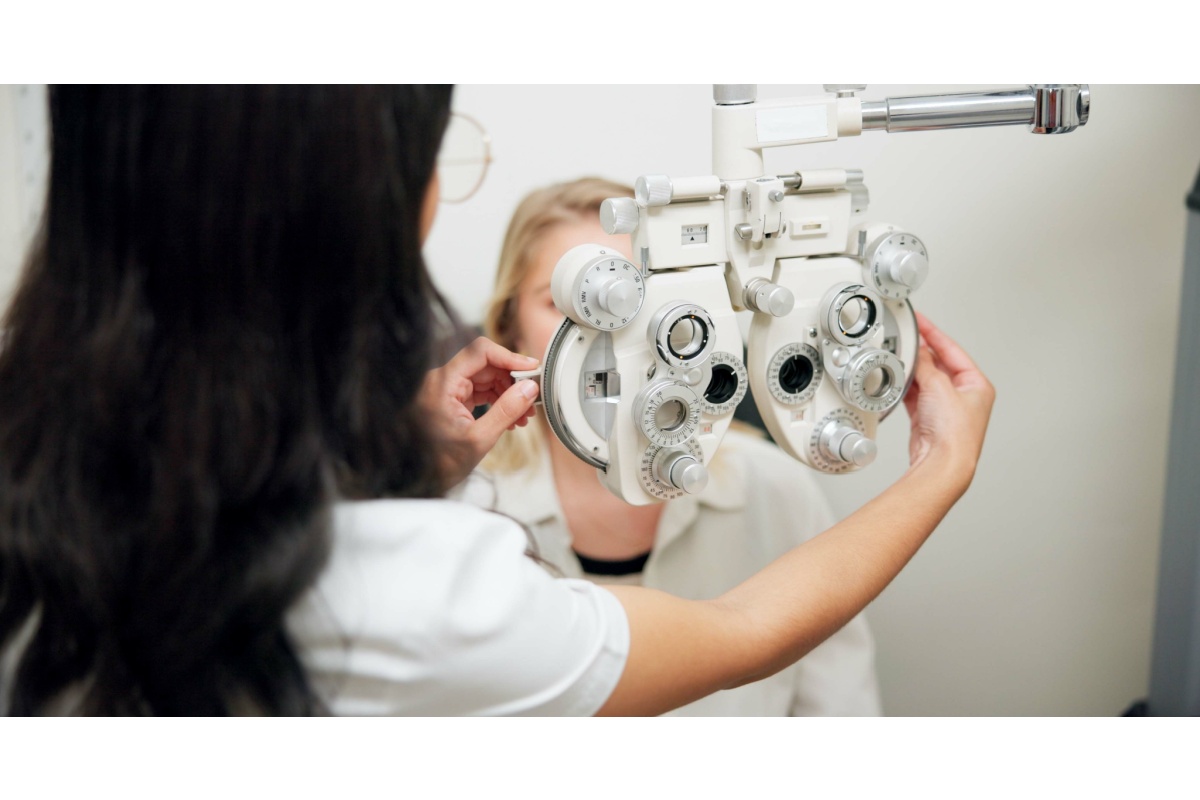 Optometrist adjusting a phoropter while a patient undergoes a vision and eye exam in a clinic.