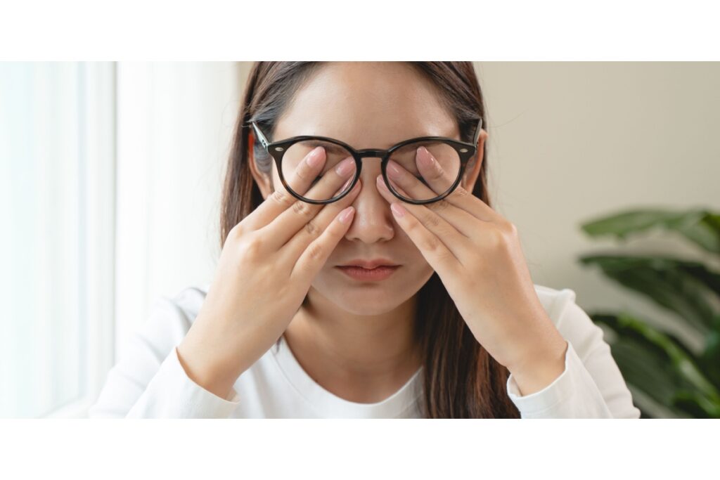Woman rubbing her eyes under her glasses due to dry eye discomfort.
